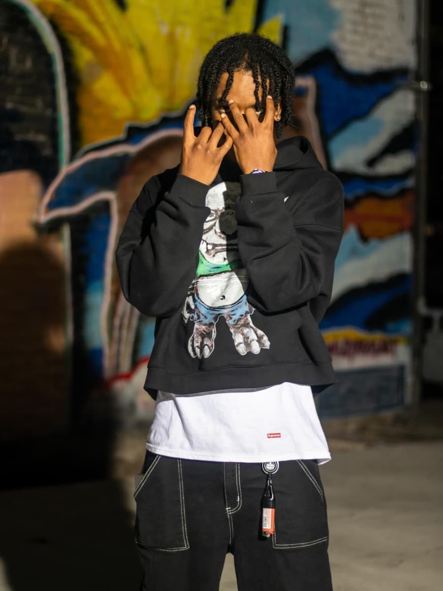 $EN! photographed against a graffiti wall, hands raised to his face