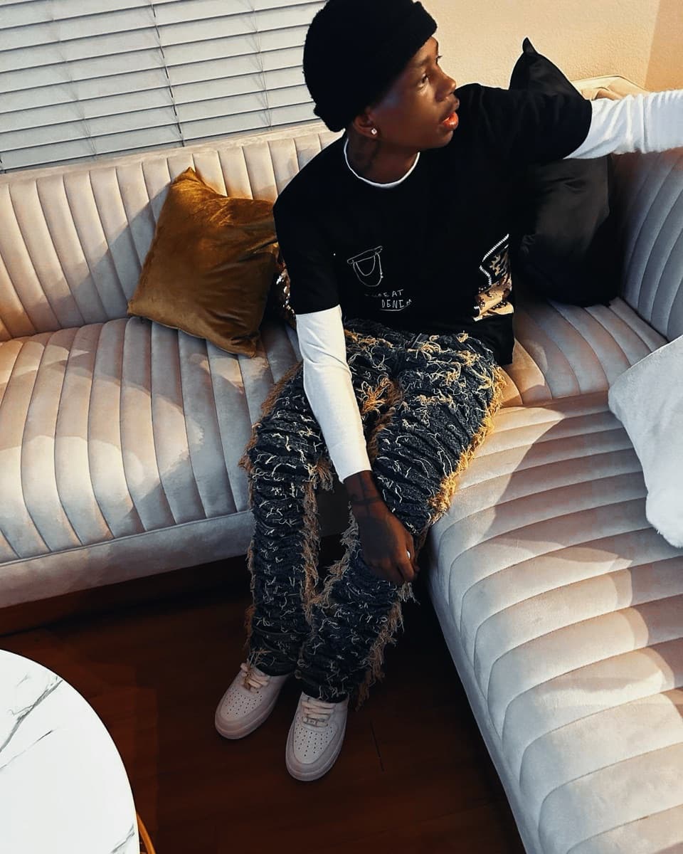 VUDO seated on a couch in a black beanie and distressed denim